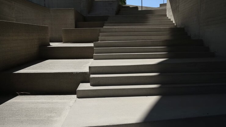 Concrete Steps Bathed In Stark Sunlight Reveal Sharp Geometric Shadows Across Brutalist Stairwell, Minimal