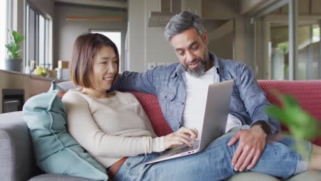 happy diverse couple sitting in living room using laptop and talking