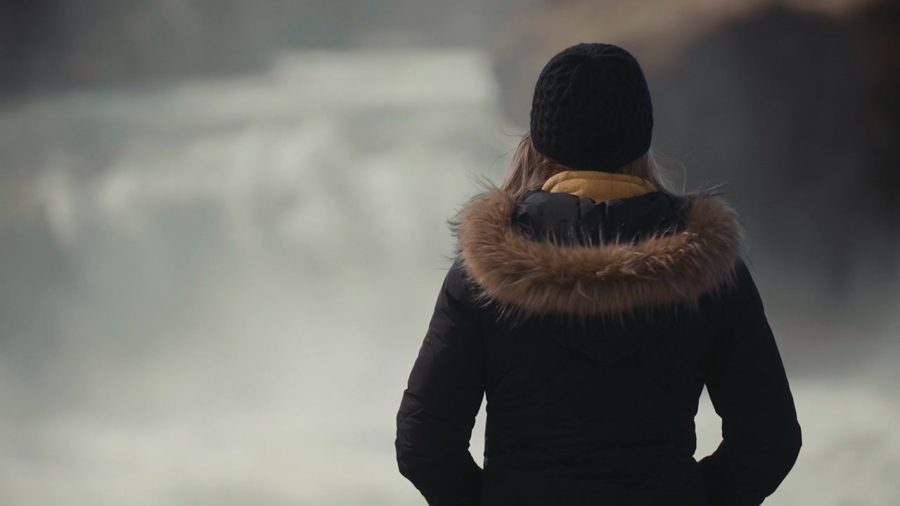 Woman in Winter Jacket Looking at a Powerful Waterfall