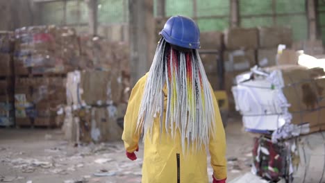 planta de procesamiento de residuos. reciclaje y almacenamiento de residuos para su posterior eliminación. trabajadora con casco de seguridad, guantes caminando por