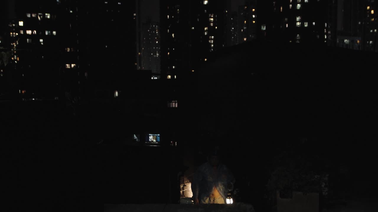 человек в синем пластиковом плаще, держащий светящийся фонарь в городе ночью