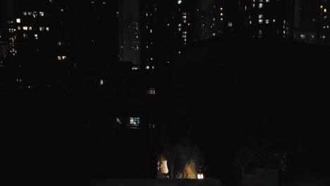 a man wearing a blue plastic raincoat, holding a glowing lantern in a city at night