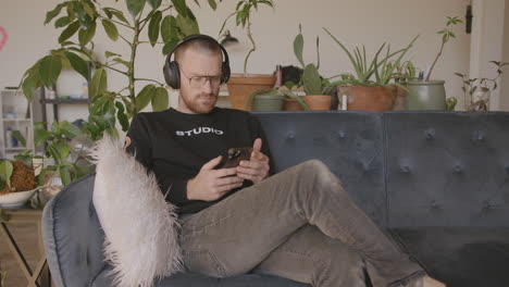 medium close front angle of a man sitting on a couch scrolling and swiping and typing on an iphone