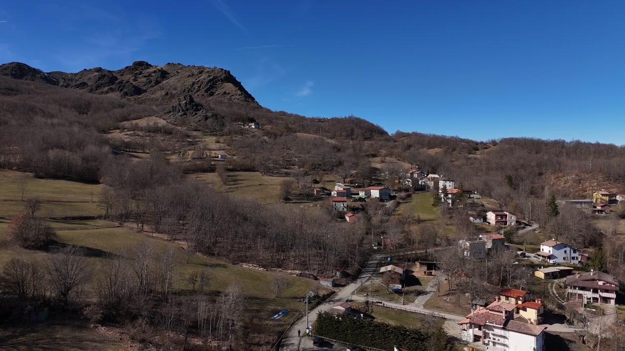 Piccolo borgo rurale vicino a Monte Lama nell'Appennino settentrionale dell'Emilia Romagna, Italia, circondato da boschi di montagna, campi terrazzati e case isolate in collina. Ripresa aerea del paesaggio con drone.