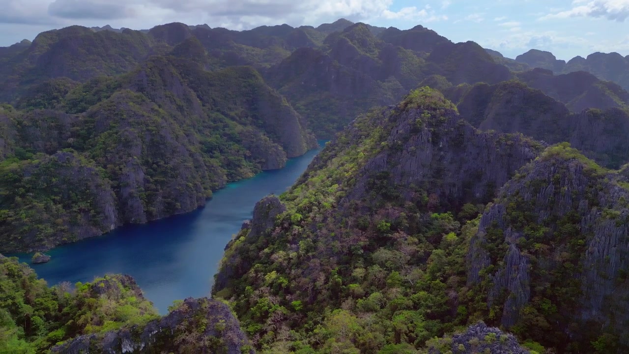 Yemyeşil bitki örtüsüyle kaplı, yüksek kireçtaşı karstlarla çevrili gizli bir lagünün turkuaz suyu olan Kayangan Gölü. Sola doğru dönen, büyüleyici bir havadan drone panoraması.