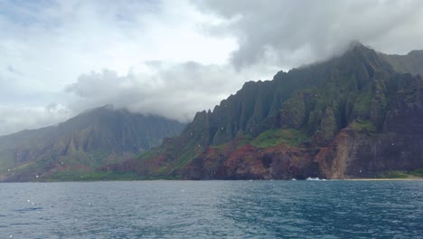 4k-Hawaii-Kauai-Bootfahren-Auf-Dem-Ozean,-Von-Links-Nach-Rechts-Schwebend,-Mit-Strand-Und-Bergen-Entlang-Der-Felsigen-Küste-Mit-Bootsgischt-Im-Vordergrund