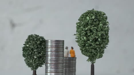 old age miniature people on a pile of coins between miniature trees.