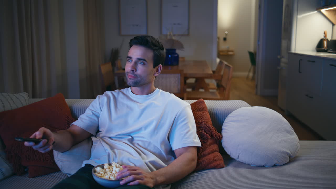 Tilskuer ser en morsom film på TV fra en koselig leilighetssofa nærbilde. Smilende fyr