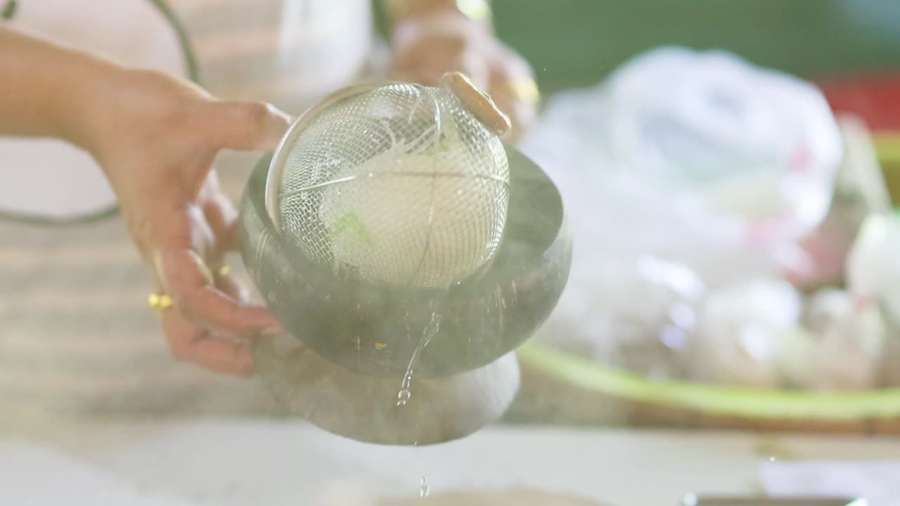 A vendor strains steaming noodles into a rustic wooden bowl at a market stall.