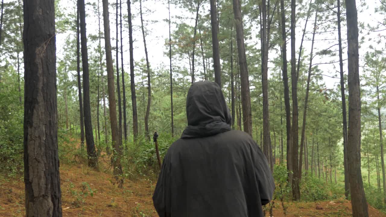 tiro de seguimiento desde atrás en cámara lenta de un cazador africano acechando a través de un bosque de pinos con un arco y una flecha