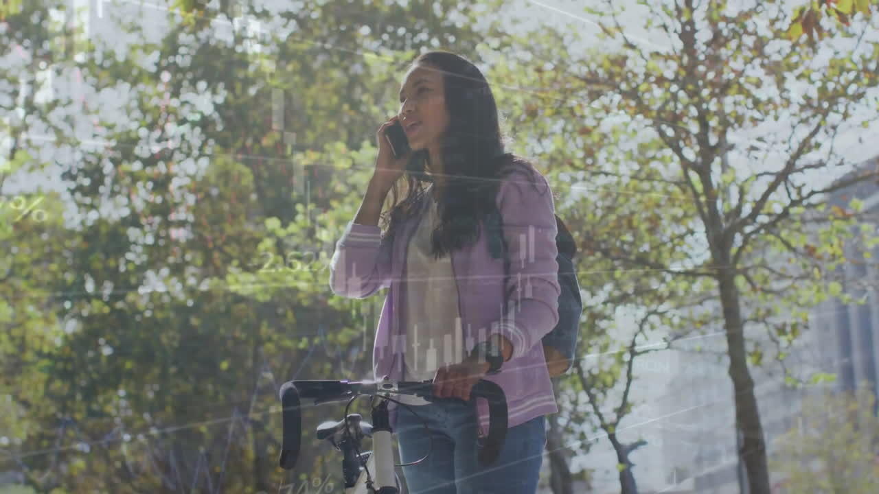 animación de procesamiento de datos en gráfico sobre mujer biracial con bicicleta hablando por teléfono en el parque de la ciudad