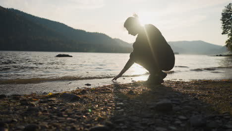 woman touches lake water at back sunset. lady tries to find inner peace in solitude with wild nature travelling alone. calmness atmosphere at twilight