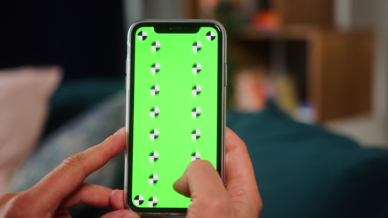 primer plano de una mano de hombre sosteniendo una maqueta verde pantalla clave de croma teléfono inteligente. teléfono móvil en el fondo atmósfera acogedora de loft casero