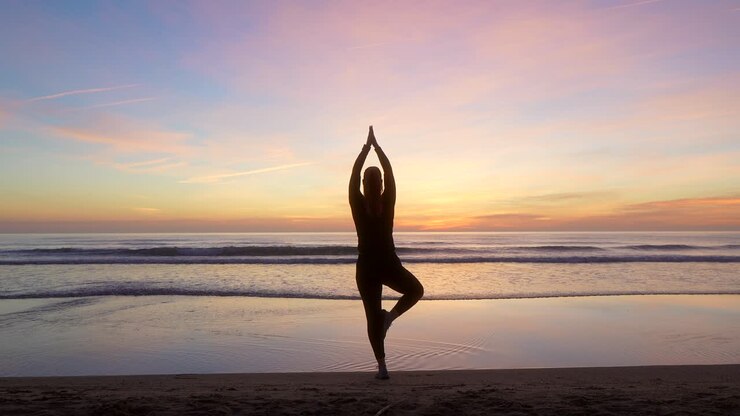 silhouette di donna che fa la posa dell'albero guardando verso il mare