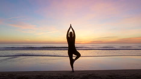 silhouette of woman doing tree pose looking towards the sea