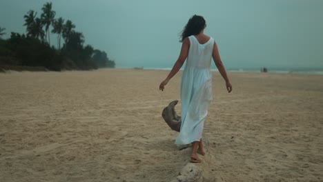 Frau-Im-Weißen-Kleid-Geht-In-Der-Abenddämmerung-Am-Strand-Entlang,-Sanfte-Brise-In-Ihren-Haaren,-Heitere-Stimmung