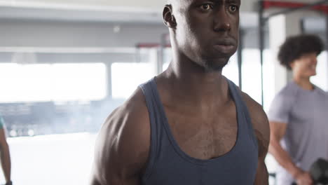 young african american man in gym wearing blue tank top, training with weights