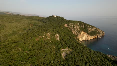 beautiful cape covered in green forest, flying over old monastery with sea view in mediterranean coast