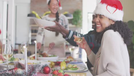 Animation-of-hearts-over-diverse-friends-sitting-at-table-at-christmas