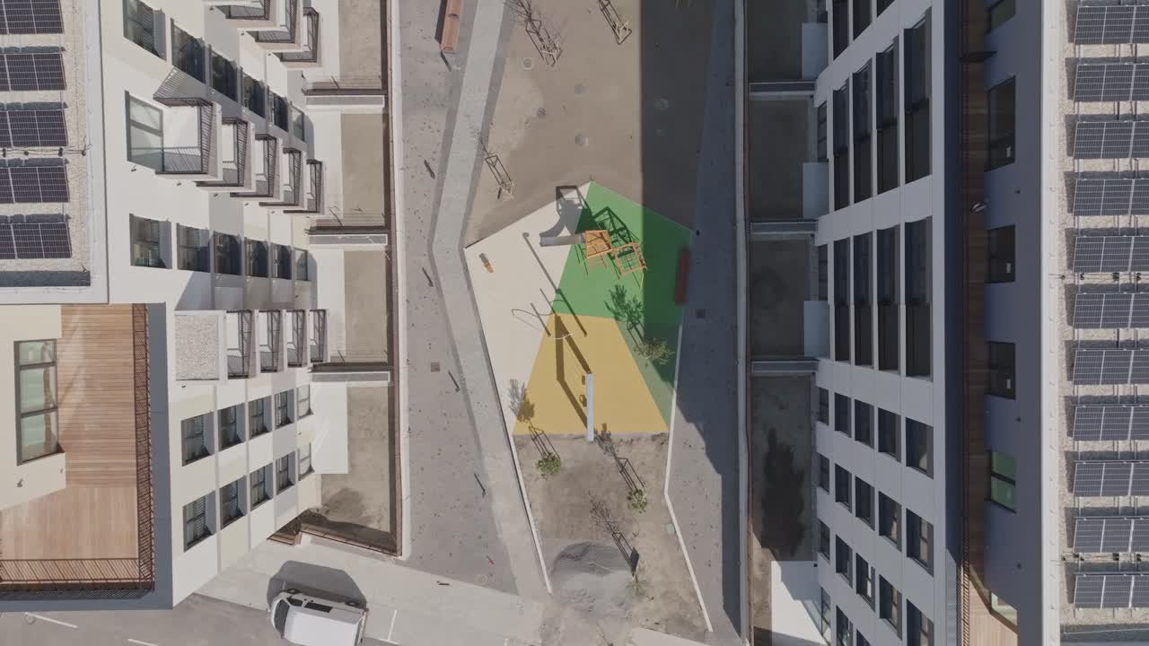 Colourful playground in newly built apartments with solar photovoltaic panels on the roof. Modern living concept. Real estate building from above. Aerial top down view. (4K)