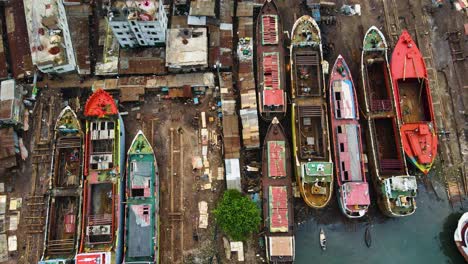 aerial: rusty abandoned cargo ships for repair at dockyard beside slum community in asia