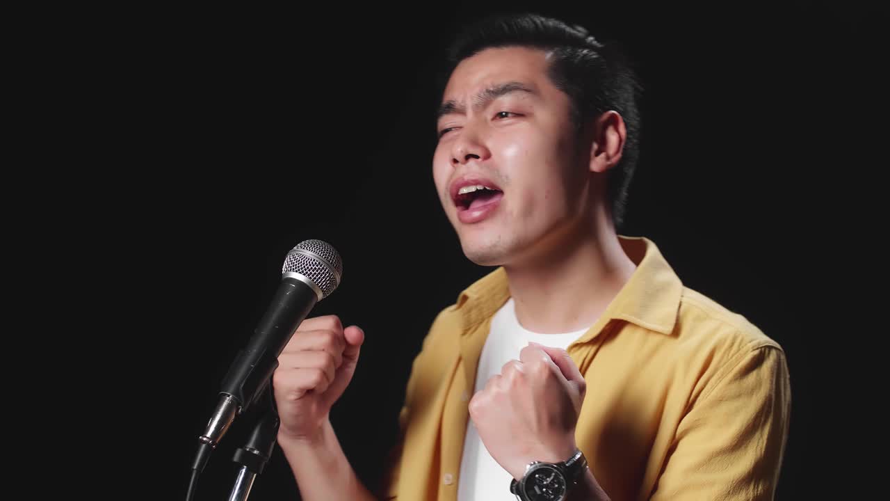 Side View Of Asian Man Singer Singing Into Microphone On Black Background