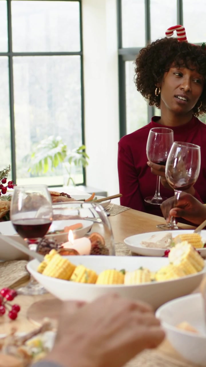 Vertical video: Lifting two wineglasses, woman in festive headband answering right speaker at home
