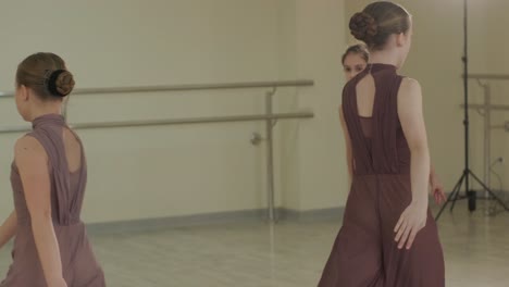 a group of young ballet students in black dancewear practicing positions in a spacious ballet studio with wooden flooring and wall-mounted barres. focused expressions and synchronized movements.