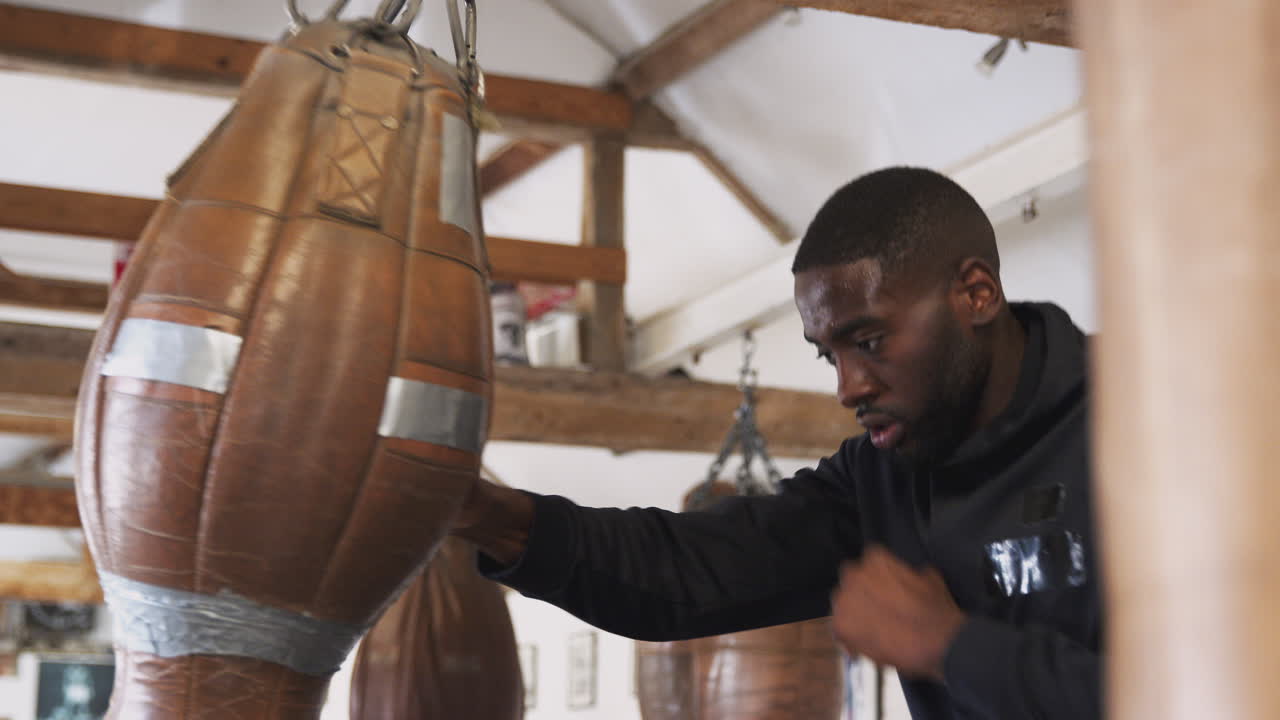 boxeador masculino en entrenamiento de gimnasio con un saco de boxeo anticuado