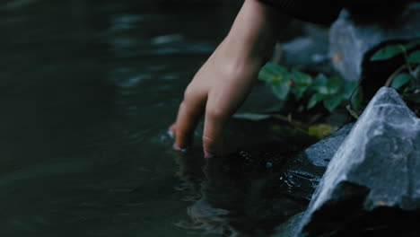 Cerrar-La-Mano-De-Una-Mujer-Salpicando-Agua-Disfrutando-De-Tocar-Un-Arroyo-Fresco-En-La-Naturaleza-Al-Aire-Libre