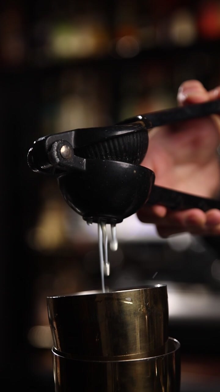Primo piano di una mano che spreme succo di agrumi fresco in uno shaker da cocktail