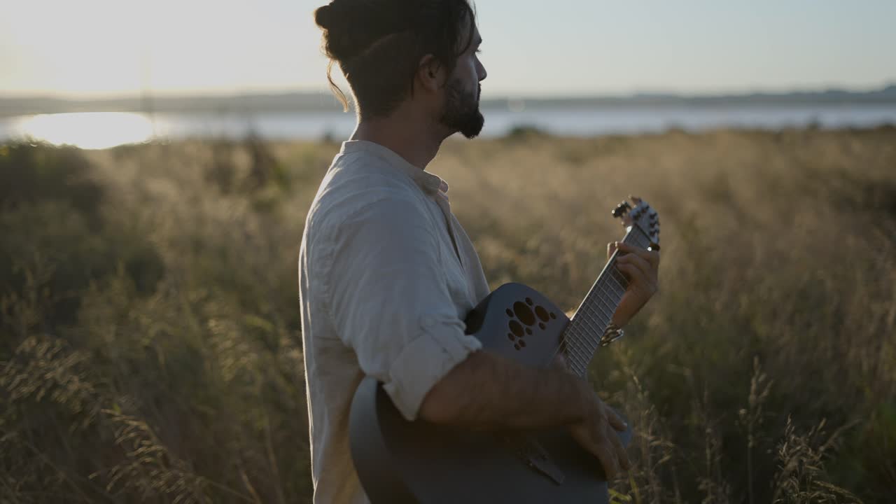 Man playing acoustic guitar in a field at sunset