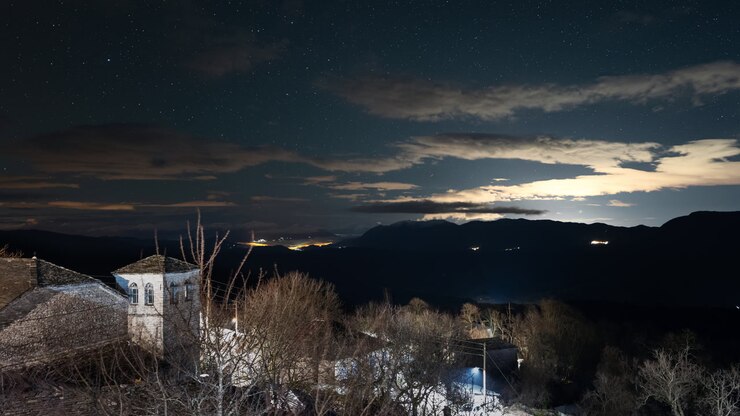 A serene night scene of Zagori village under a starry sky, with distant lights illuminating the horizon. Ideal for travel and nature themes.