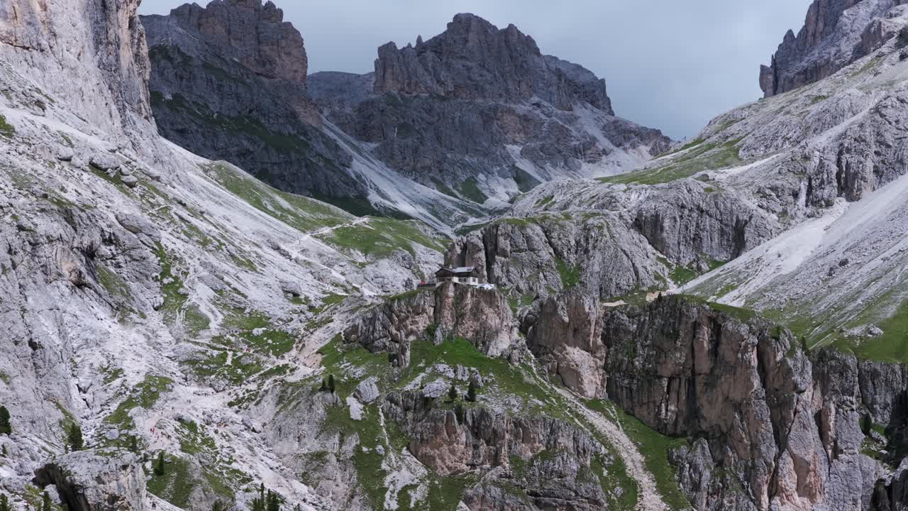 A house atop a rocky outcropping with Vajolet towers mountain peaks background