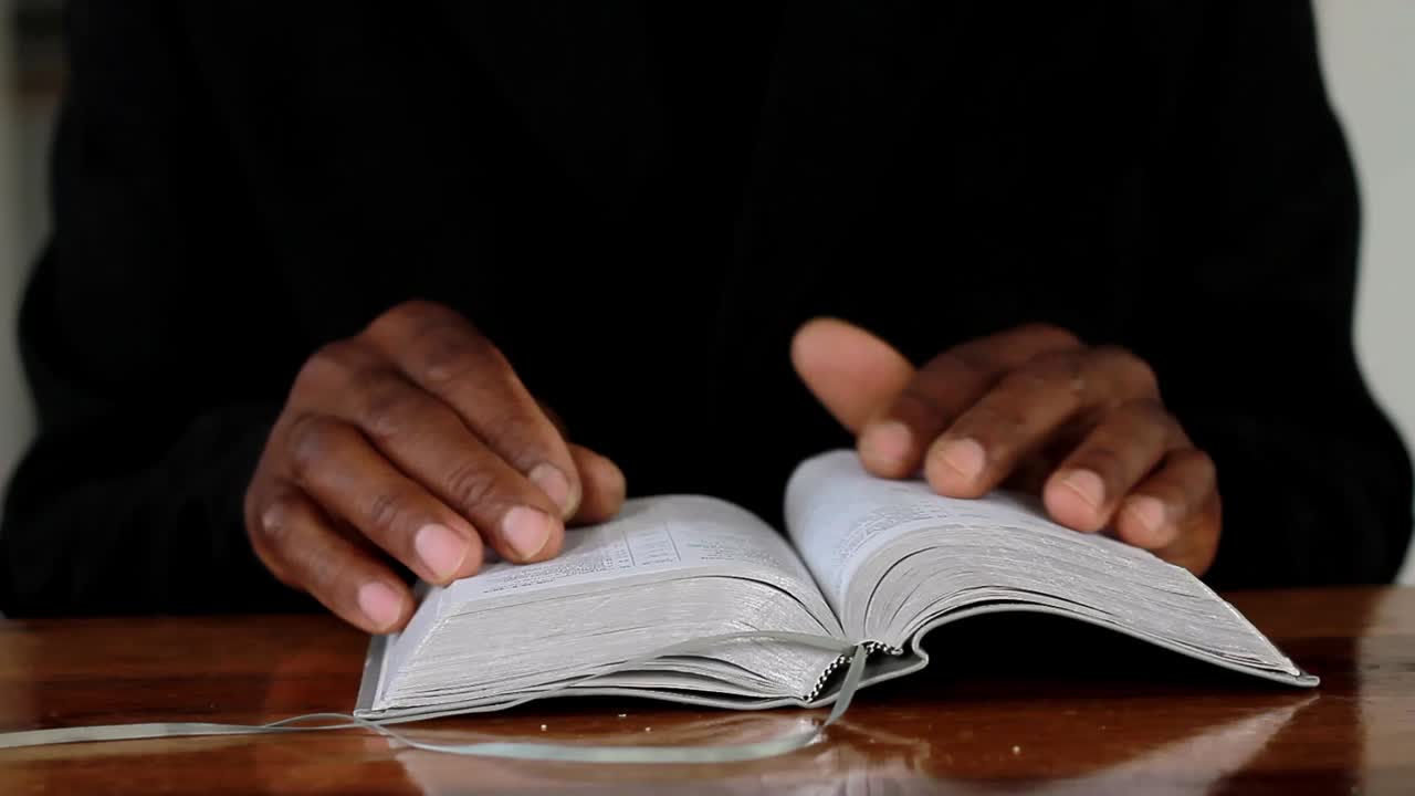 hombre rezando con la mano en el fondo negro de la biblia metrajes