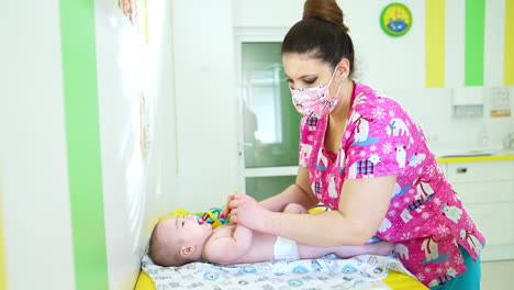 female pediatrician examining a naked toddler in a diaper. doctor is touching the baby to check his health and growth.