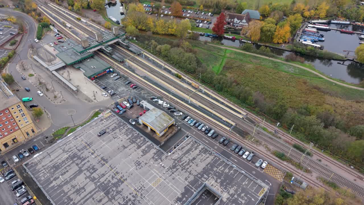 Drone orbit over Harlow Town train station, capturing platforms, tracks, and local car park. Harlow Marina and canal boats are in the background, showing a complete aerial perspective
