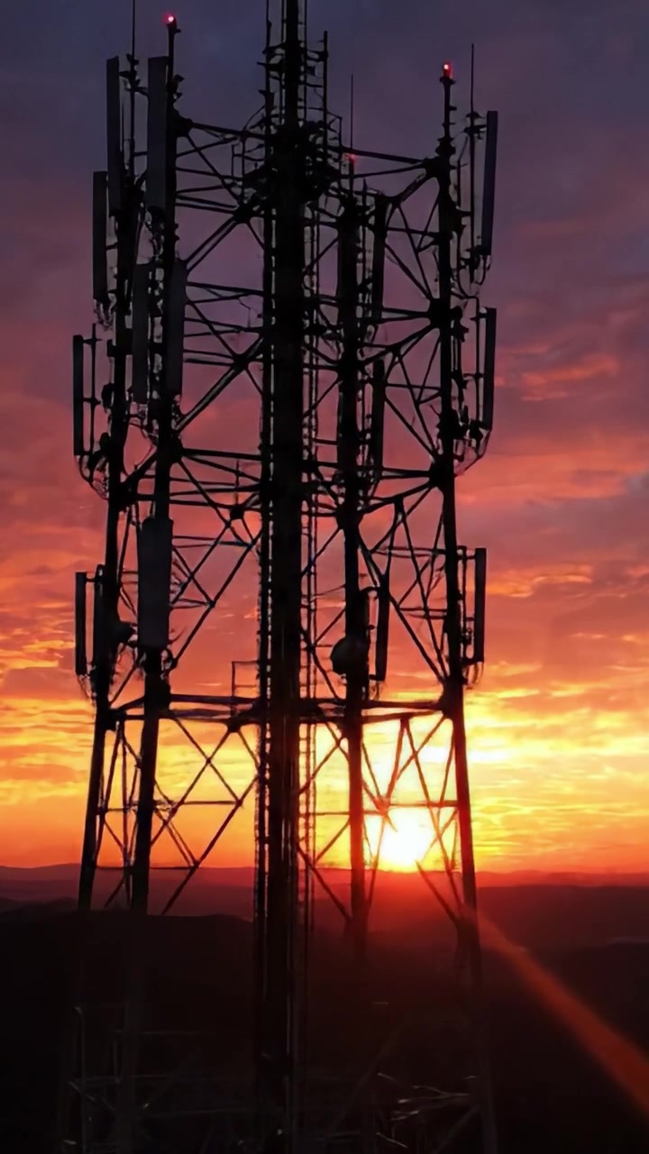 Un tramonto mozzafiato dietro una torre di trasmissione radio, che illumina il cielo con vivaci sfumature di arancione, rosa e viola mentre il giorno si trasforma in notte