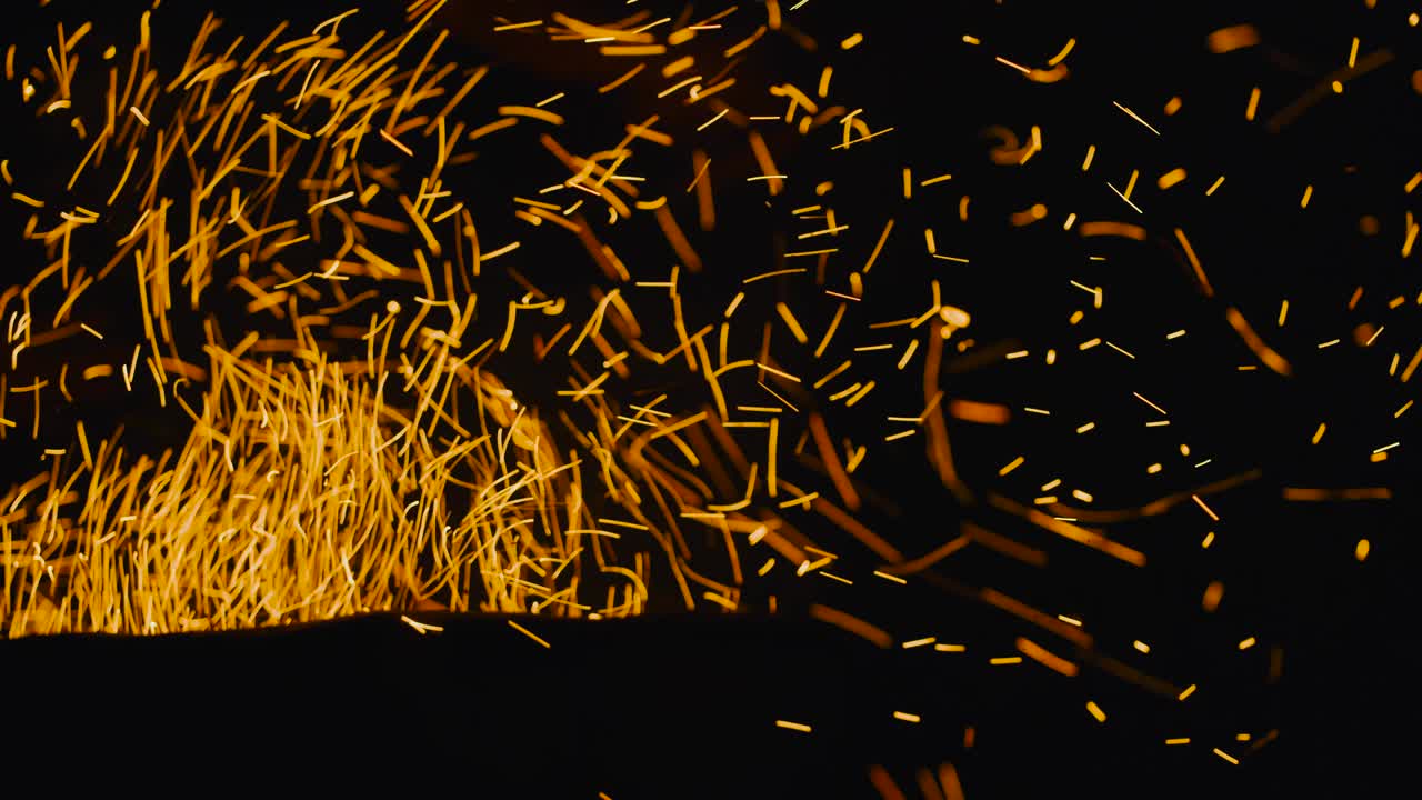 Burning red hot sparks rise from fire in the night sky