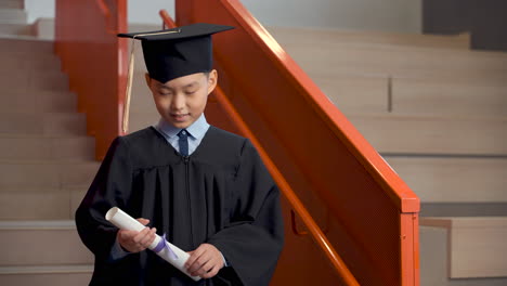 happy preschool male student in cap and gown holding diploma and celebrating his graduation 1