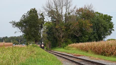 view of a steam passenger train approaching slowly along a single track in rural america on a fall day