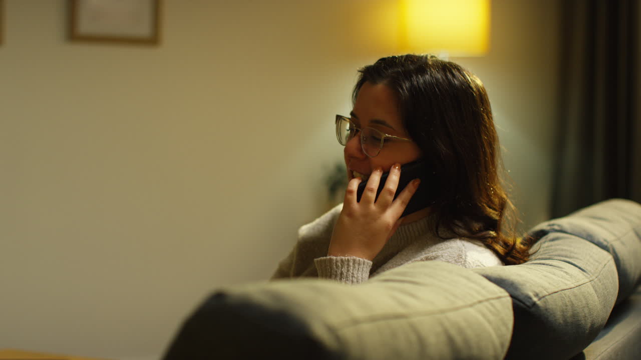 Young Woman Spending Evening At Home Sitting On Sofa Talking On Mobile Phone
