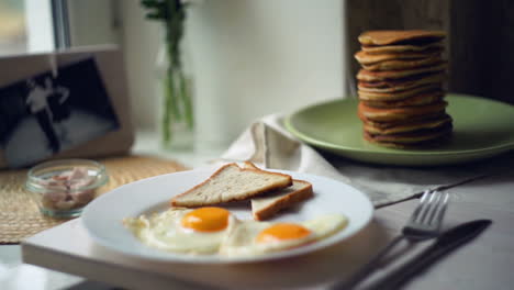 Breakfast-plate.-Fried-eggs-with-bread-toasts-and-pancake-stack-on-kitchen-table