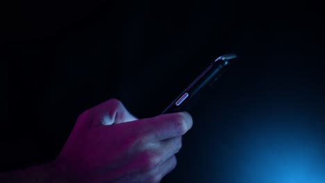 Desplazamiento-Del-Pulgar-En-Un-Smartphone-En-Una-Habitación-Oscura-Con-Iluminación-Violeta-Y-Azul