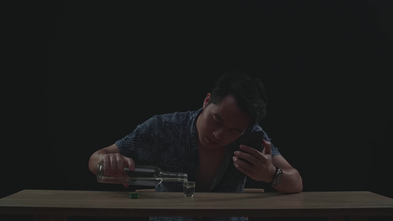 Asian Man Pouring Vodka In A Shot Glass Before Drinking During Having Video Call In Black Background