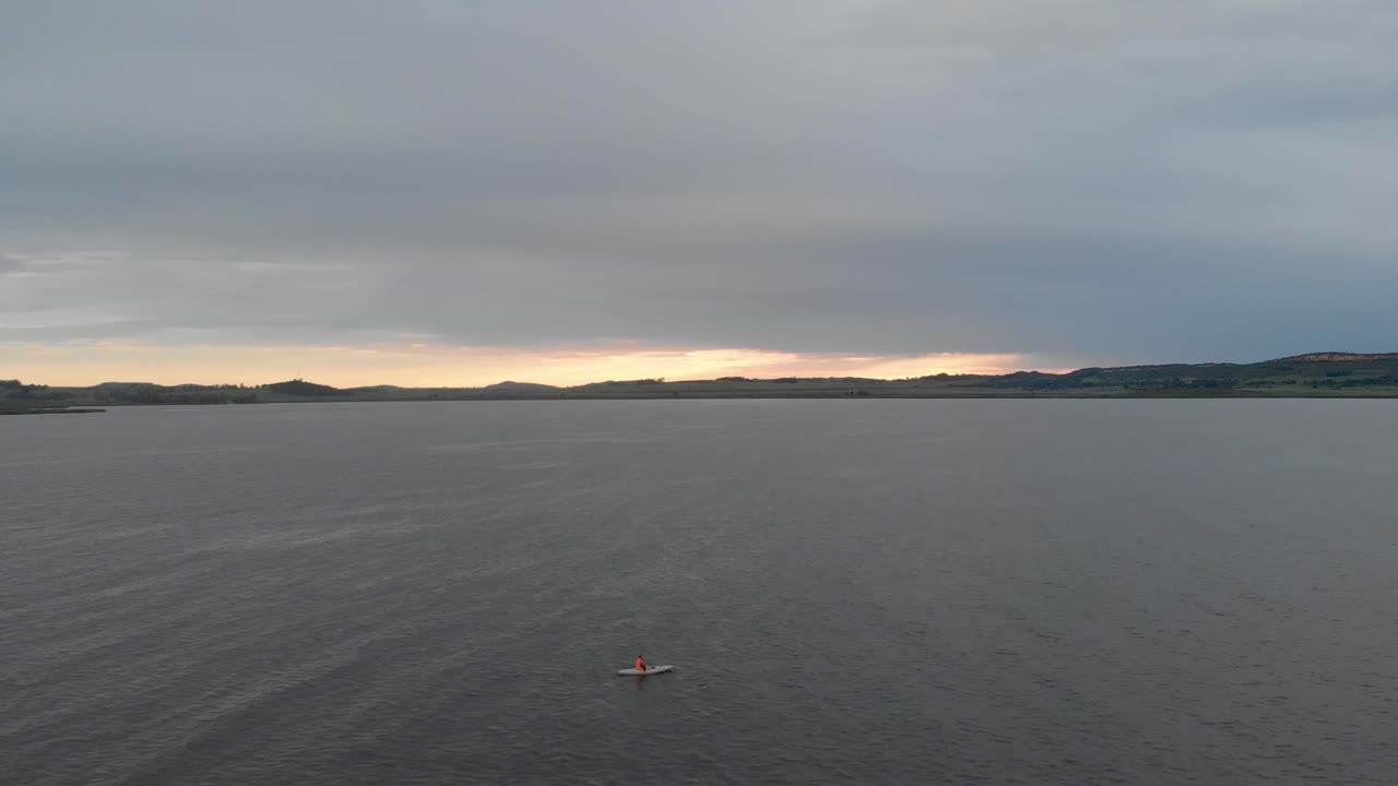 수평선 위로 떠오르는 태양과 함께 빅토리아 호수에서 카약을 타고 외로운 남자 위로 앞으로 이동하는 공중 샷