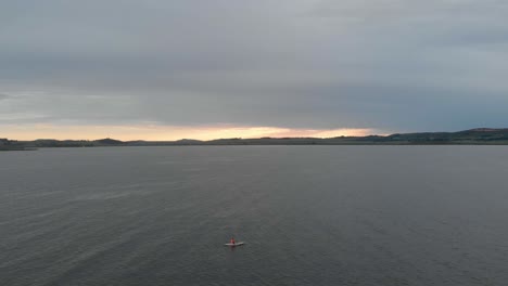 Toma-Aérea-Avanzando-Sobre-Un-Hombre-Solitario-En-Un-Kayak-En-El-Lago-Victoria-Con-El-Sol-Saliendo-En-El-Horizonte