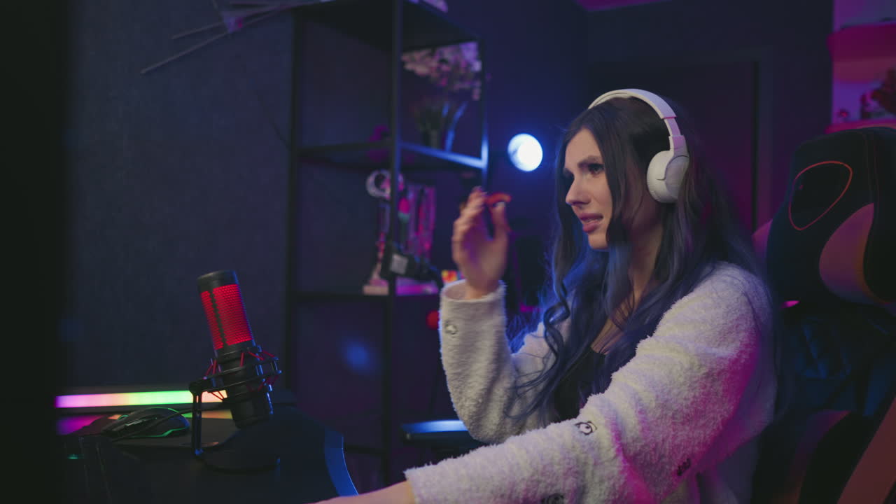 Frustrated freelancer wearing white headset sits in creative studio setup with dim lighting, reacting to challenging task with visible disappointment, seated in gaming chair near condenser mic