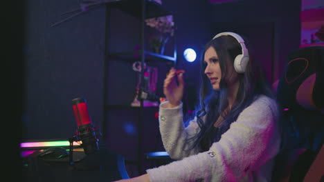 frustrated freelancer wearing white headset sits in creative studio setup with dim lighting, reacting to challenging task with visible disappointment, seated in gaming chair near condenser mic
