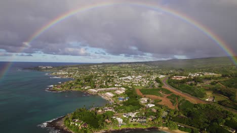 grey cloudy skies and perfect rainbow above hawaiian bay and tropical hotels